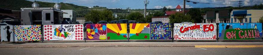 Row of mural artwork fro Canada 150 hanging on a long fence.